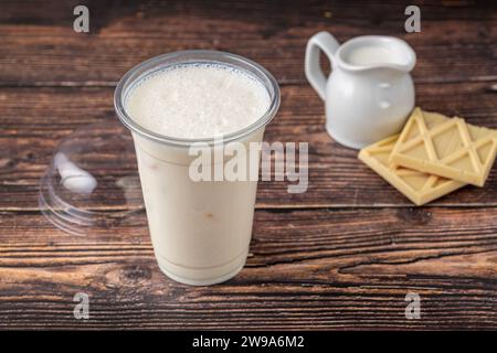 Weiße Schokoladenmilch in Take Away Glas auf Holztisch Stockfoto