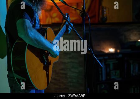 Selektiver Fokus einer Hand, die akustische Gitarre spielt und auf einem Mikrofon in Innenräumen singt Stockfoto