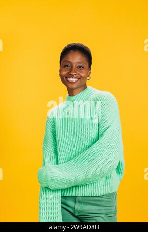 Porträt einer fröhlichen jungen, schönen Frau in grünen Kleidern, die vor gelbem Hintergrund steht. Eine junge Frau im Studio, die in die Kamera schaut. Stockfoto