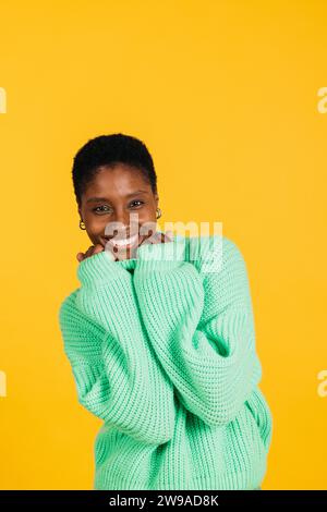 Porträt einer fröhlichen jungen, schönen Frau in grünen Kleidern, die vor gelbem Hintergrund steht. Eine junge Frau im Studio, die in die Kamera schaut. Stockfoto