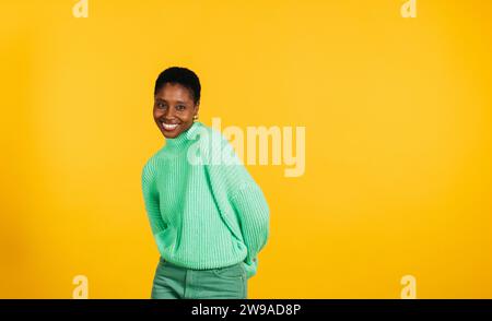 Porträt einer fröhlichen jungen, schönen Frau in grünen Kleidern, die vor gelbem Hintergrund steht. Eine junge Frau im Studio, die in die Kamera schaut. Stockfoto