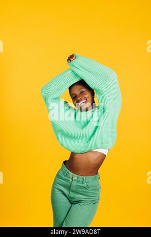 Porträt einer fröhlichen jungen, schönen Frau in grünen Kleidern, die vor gelbem Hintergrund steht. Eine junge Frau im Studio, die in die Kamera schaut. Stockfoto