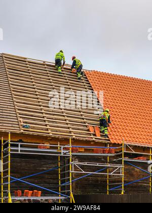 Drei Arbeiter in Schutzkleidung, die ein neues Dach aus Tonziegeln und eine neue Schicht aus Tonziegeln installieren Stockfoto