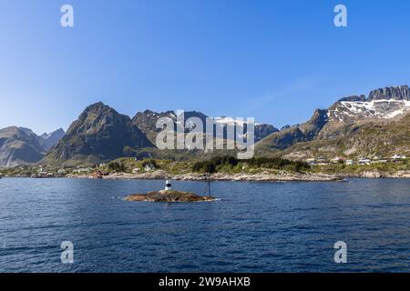 Eine ruhige Sommerszene von einer Fähre im Norwegischen Meer aus, die die majestätische Bergkette mit Holzhäusern über dem ruhigen Wasser zeigt Stockfoto