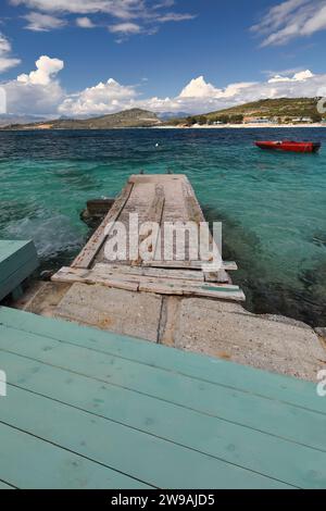 175 Betonpier in das Wasser am Strand Rilinda, rotes Außenbordboot auf dem rechten Hintergrund, Dorf Ksamil. Sarande-Albanien. Stockfoto