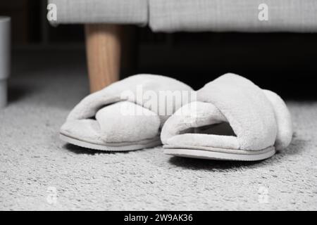 Moderne graue Hausschuhe auf dem Teppich in der Nähe des Sofas. Bequeme und bequeme Schuhe für zu Hause Stockfoto