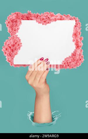 Weibliche Hand, die leeres Papier hält, bedeckt mit pinkfarbenen Tintenspritzern auf pastellblauem Hintergrund. Kopieren Bild für Text einfügen. Stockfoto