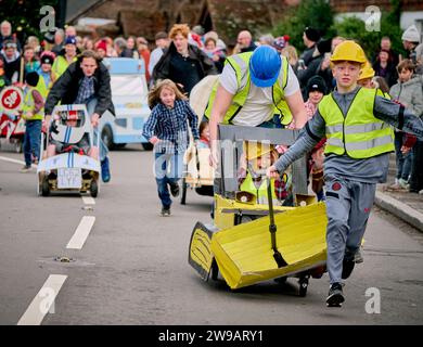 East Hoathly, Großbritannien. Dezember 2023. Kinderwagenrennen am Boxing Day: Teams in schicken Kleidern laufen durch das Dorf East Hoathly in East Sussex und sammeln Spenden für lokale Wohltätigkeitsorganisationen. Die jährliche Veranstaltung beginnt und endet im Kings Head Pub im Zentrum des Dorfes. Quelle: Jim Holden/Alamy Live News Stockfoto
