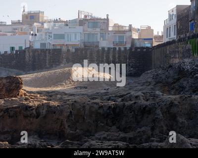 Ecke eines Sandstrandes mit großen Felsen neben den Stadtmauern und der historischen Medina in Essaouira, Marokko. Dezember 2023 Stockfoto