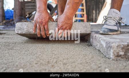 Installation von neuem Bürgersteig oder Boden im Außenbereich von großen Betonfliesen, Nahaufnahme von männlichen Arbeitern, die Steinblöcke über Sand und Kies montieren. Stockfoto