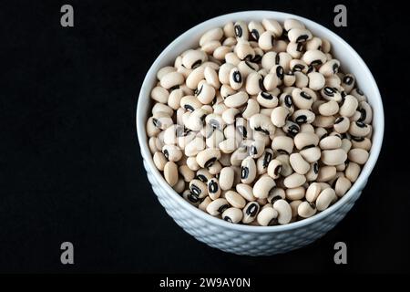 Schwarze Augenerbsen in einer weißen Schüssel auf schwarzem Hintergrund, Draufsicht. Schwarze Bohnen, auch bekannt als Kuherbsen. Stockfoto