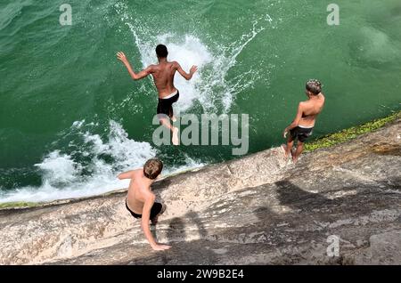 Rio de Janeiro, Rio de Janeiro, Brasilien. Dezember 2023. Eine Gruppe junger Männer springt von Felsen am Pier am Leme Beach in Rio de Janeiro. Angesichts des starken Anstiegs des Index auf dreifache Zahlen versuchen Einheimische und Touristen gleichermaßen, am Tag vor dem Neujahrsfest der Copacabana cool zu bleiben, das Millionen von Schwärmern aus der ganzen Welt anzieht. (Credit Image: © Bob Karp/ZUMA Press Wire) NUR REDAKTIONELLE VERWENDUNG! Nicht für kommerzielle ZWECKE! Stockfoto