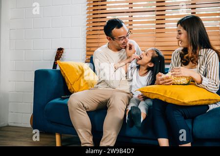 Eine glückliche Familie voller Freude schaut fern, während sie auf einem modernen Sofa zu Hause Popcorn isst Stockfoto
