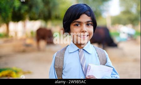 Lächelnde Schülerin mit Schulrucksack und Lehrbuch. Porträt eines glücklichen asiatischen Dorfes vor Haustieren. Das Gesicht der lächelnden Schule Stockfoto