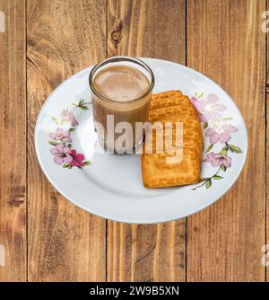 Kekse und Tee mit Milch auf Glas, Nahaufnahme Zucker Kekse Kekse auf Teller hölzernen Hintergrund. Stockfoto