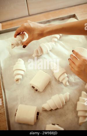 Nahaufnahme von oben, weibliche Hände legen Gebäck, Croissants und Brot mit Tassen Schokolade. Rezepte, Traditionen. Stockfoto