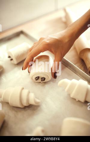 Nahaufnahme: Weibliche Hände legen Gebäck, Croissants und Brot mit Schokoladenriegeln in selektiver Fokussierung auf. Konzept französischer Dessertrezepte. Stockfoto