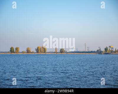 Eine große Vogelschar, die über der Kiewer Meeresspieße fliegt, ruhiges blaues Wasser mit Jacht und Boot, blauer und rosafarbener Himmel, schmaler Uferstreifen am Horizont Stockfoto