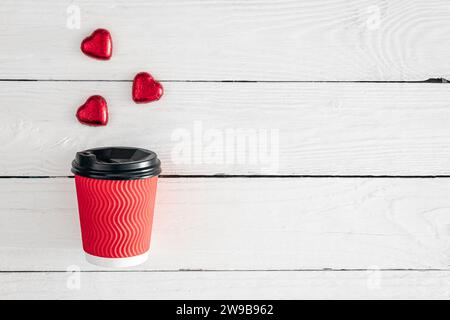 Roter Papierbecher und herzförmige Süßigkeiten auf weißem Holzhintergrund. Stockfoto