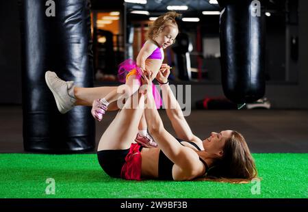 Die charmante Sportmutter spielt im Fitnessstudio mit ihrer kleinen Tochter. Gemischte Medien Stockfoto