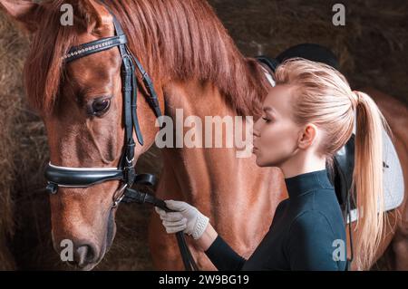 Atemberaubende Blondine posiert mit einem Vollblutpferd. Ranch-Urlaubskonzept. Gemischte Medien Stockfoto