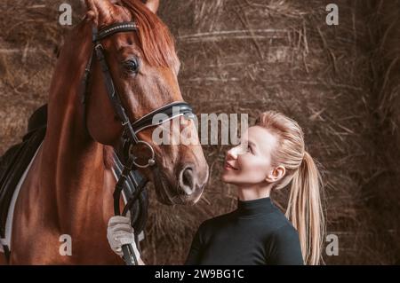 Atemberaubende Blondine posiert mit einem Vollblutpferd. Ranch-Urlaubskonzept. Gemischte Medien Stockfoto