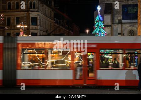 26. Dezember 2023, Sachsen-Anhalt, Halle (Saale): In den Fenstern einer vorbeifahrenden Straßenbahn spiegeln sich die Lichter des 13. Halleschen Wintermarktes. Der Markt im Stadtzentrum ist bis 7. Januar 2024 geöffnet. Foto: Heiko Rebsch/dpa Stockfoto