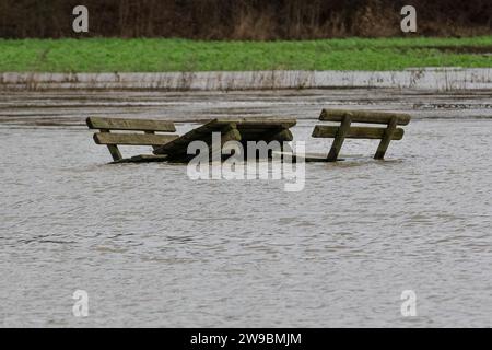 Olfen, NRW, Deutschland. Dezember 2023. Ein Picknicktisch und Bänke, die normalerweise an Land stehen, scheinen im Wasser zu sinken. Der Fluss Stever und seine Seitenarme haben große Teile der umliegenden Landschaft stark überflutet. In der Nähe der Stever Bridge, einer historischen Dreibogenbrücke, die früher kleine Boote in einem Kanal über den Fluss Stever transportierte (heute eine Fußbrücke), sind die umliegenden Felder knietief überflutet. Weite Teile Nord- und Westdeutschlands haben nach wochenlangen Starkregen Überschwemmungen erlebt. Die Prognose ist für mehr Regen. Quelle: Imageplotter/Alamy Live News Stockfoto