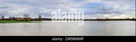 Olfen, NRW, Deutschland. Dezember 2023. Multi-Bild-Panorama-Stich. Der Fluss Stever und seine Seitenarme haben große Teile der umliegenden Landschaft stark überflutet. In der Nähe der Stever Bridge, einer historischen Dreibogenbrücke, die früher kleine Boote in einem Kanal über den Fluss Stever transportierte (heute eine Fußbrücke), sind die umliegenden Felder knietief überflutet. Weite Teile Nord- und Westdeutschlands haben nach wochenlangen Starkregen Überschwemmungen erlebt. Die Prognose ist für mehr Regen. Quelle: Imageplotter/Alamy Live News Stockfoto