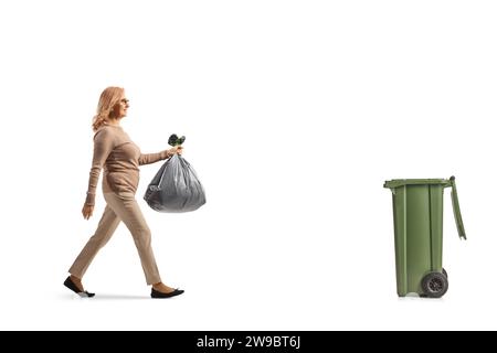 Profilaufnahme einer Frau mittleren Alters, die einen Plastikmüllbeutel trägt und zu einem Abfalleimer auf weißem Hintergrund geht Stockfoto