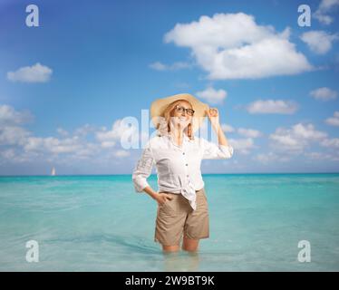 Frau mittleren Alters mit Strohhut, die im Meer posiert Stockfoto