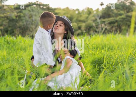 Lateinische Familie, junge Mutter mit ihren beiden Kindern, die auf dem hohen Gras sitzen und Zeit miteinander verbringen Stockfoto