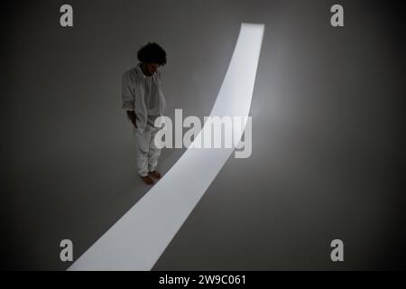 Weite Aufnahme eines Mannes, der im Schatten vor dem Lichtstreifen im Studio steht Stockfoto