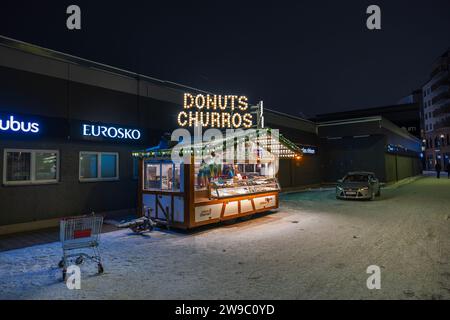 Nahaufnahme eines Straßenkiosks mit Donuts und Churros, die an einem Winterabend beleuchtet werden. Stockfoto