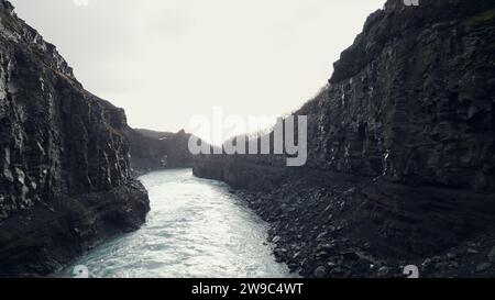 Drohnenaufnahme des nordischen Wasserfalls in island, Wasserstrom fließt in den Canyon mit gefrorenen Feldern und Landschaft. Spektakuläre isländische Landschaft mit Fluss zwischen Felsen. Zeitlupe. Stockfoto