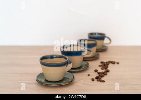 Set mit vier Tassen mit Untertassen auf einem Holztisch. Hochwertige Fotos. Handgefertigte Töpferwaren Stockfoto