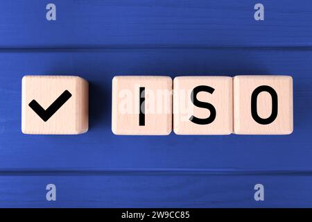 Internationale Organisation für Normung. Würfel mit Häkchen und Abkürzung ISO auf blauem Holztisch, flach gelegt Stockfoto