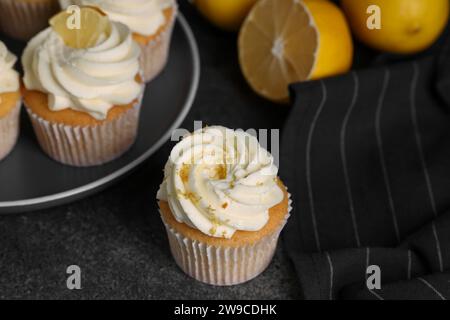 Köstliche Cupcakes mit weißer Creme, Zitronenschale und Zitronen auf grauem Tisch, Nahaufnahme Stockfoto