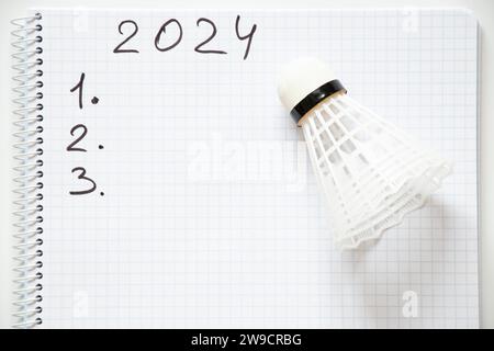 2024 und die Zahlen 123 sind in einem Notizbuch geschrieben und daneben liegt ein Shuttlecock auf weißem Hintergrund, der das neue Jahr plant Stockfoto