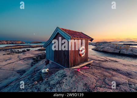 Holzhütte in der glühenden Dämmerung bei Dämmerung auf den Felsen im Naturschutzgebiet Tjurpannan im Archipel der schwedischen Westküste Stockfoto