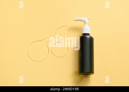 Eine unbeschriftete schwarze Lotionspumpe-Flasche, ein paar Tropfen durchscheinender, dichter Textur auf gelbem Hintergrund. Hautpflegemittel, glättendes Serum. Leerspac Stockfoto