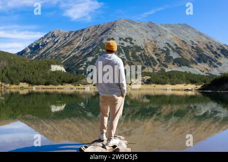 Junger Mann, der in der Nähe des Sees und der Berge steht und den Blick auf die Natur genießt Stockfoto