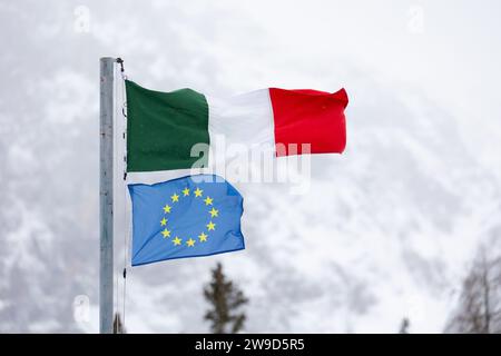 Die Fahnen Italiens und der EU (Europäische Union) fliegen zusammen vor dem Hintergrund der verschneiten italienischen Berge. Dolomiten im Winter. Stockfoto