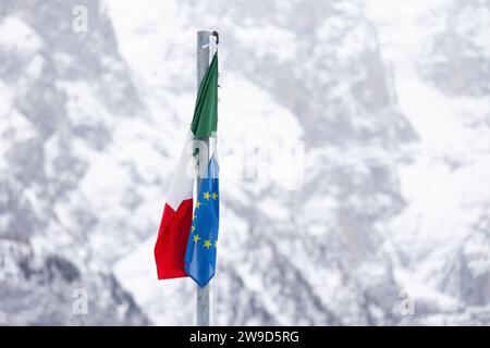 Die Fahnen Italiens und der EU (Europäische Union) fliegen zusammen vor dem Hintergrund der verschneiten italienischen Berge. Dolomiten im Winter. Stockfoto