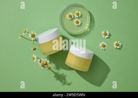 Zwei gelbe Gläser Behältercreme oder Maske mit Kamillenblüten auf grünem Hintergrund verziert. Nicht für Design beschriftet. Mockup für Werbung Cosmet Stockfoto