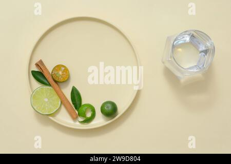 Eine runde Keramikschale mit Limetten- und Kumquatscheiben, grünen Blättern und getrockneten Zimtstäbchen, dekoriert mit einer Glasschale Wasser. Platz für Desig Stockfoto