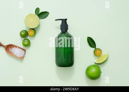 Ein Shampoo oder Duschgel mit einer Pumpflasche, dekoriert mit Limettenscheiben und Kumquat, grünen Blättern und einem Holztablett mit Badesalz auf grünem Pastell-bac Stockfoto