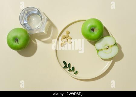 Blick von oben auf grüne Äpfel und Pillen, dekoriert mit Gegenständen auf beigem Hintergrund. Werbefotoprodukt aus grünem Apfel. Minimaler Konz Stockfoto