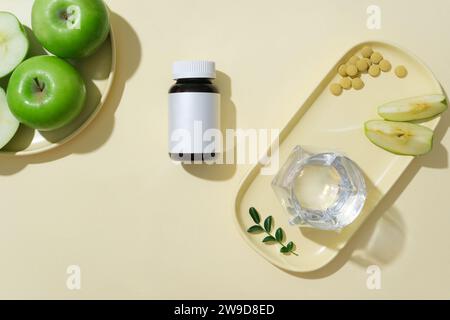 Eine Arzneiflasche auf beigefarbenem Hintergrund mit grünen Äpfeln und Pillen. Konzept für Werbemittel mit minimalistischem Stil. Grüne Äpfel sind A Stockfoto