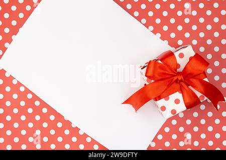 Rote Pünktchen Geschenk- oder Geschenkbox mit Schleife mit Papier auf Musterhintergrund. Geburtstag, Valentinstag, Mütter- und Frauentag, Feiertag. Kopierbereich Stockfoto